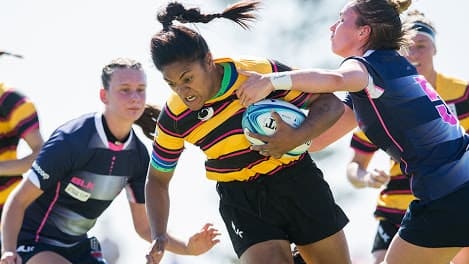 Wide shot of a female rugby player breaking a tackle.