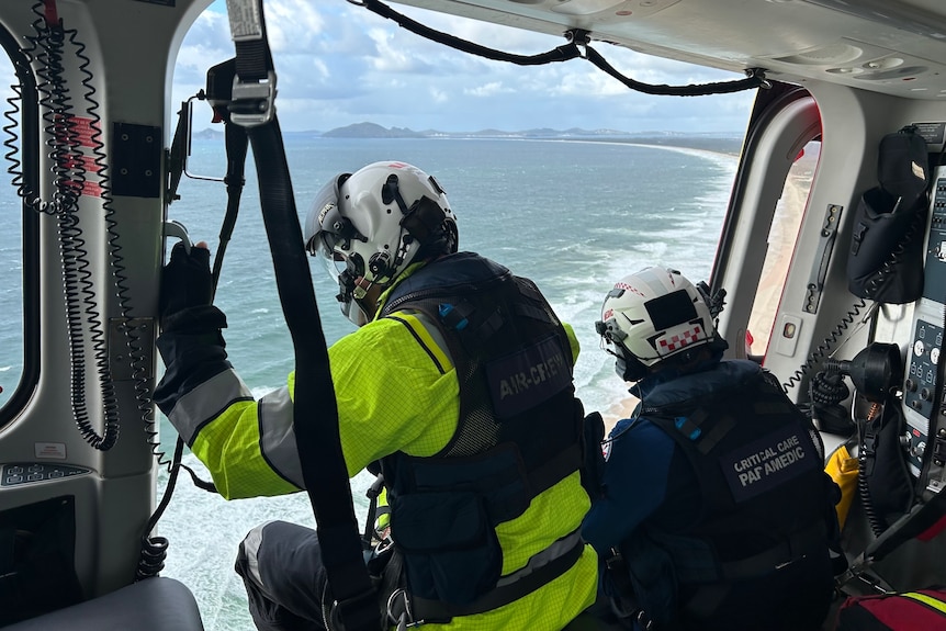 Two people in high vis in a helicopter flying over water 