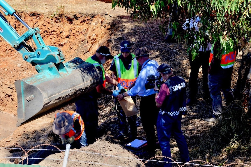 Evidence is bagged by police near a digger and partly in the shade of a tree.