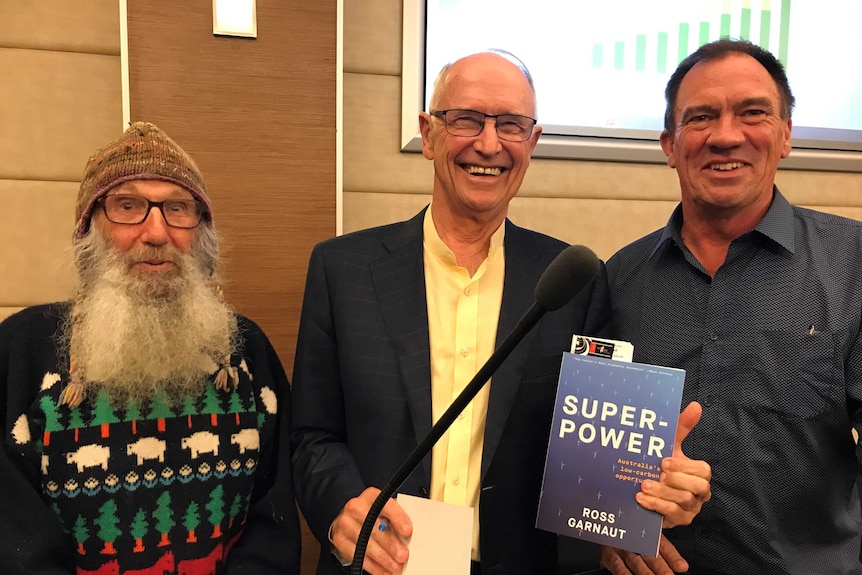 Ross Garnaut standing in the middle of a group of three men, holding a copy of his book.