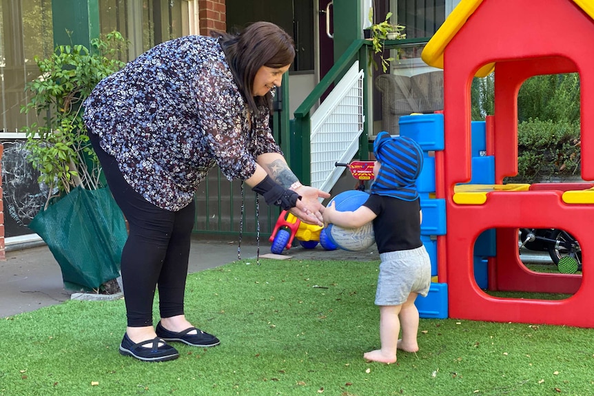 A woman plays ball with a toddler.