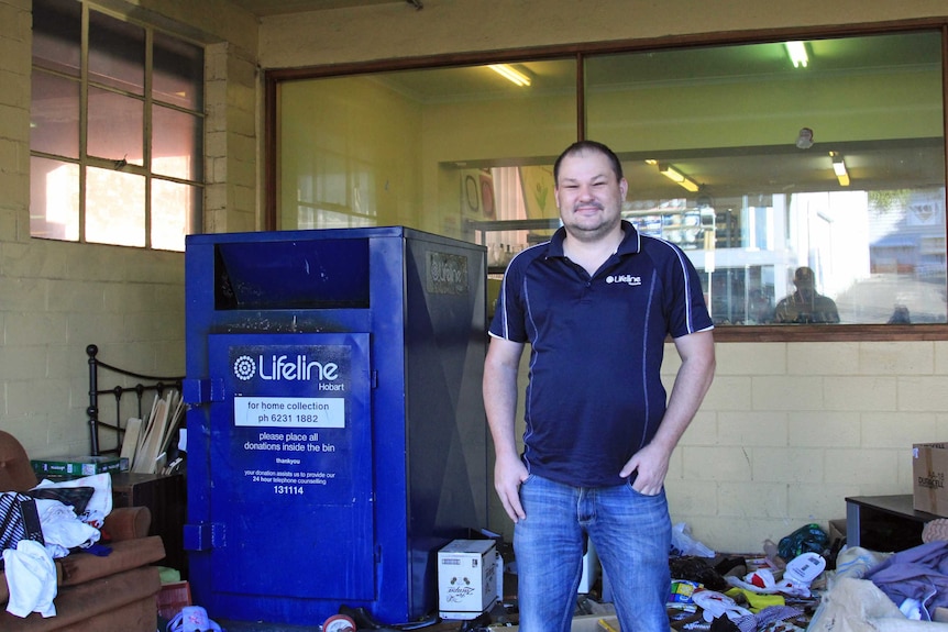 A man in a blue tshirt standing near a charity opshop bin