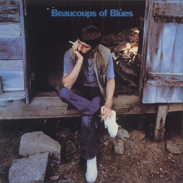 Ringo Starr sits in a barn holding a cigarette with his head in his hands.