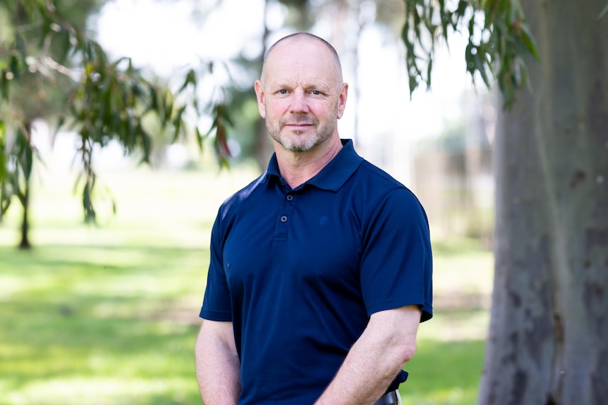 A portrait shot of a man standing in front of a tree. 