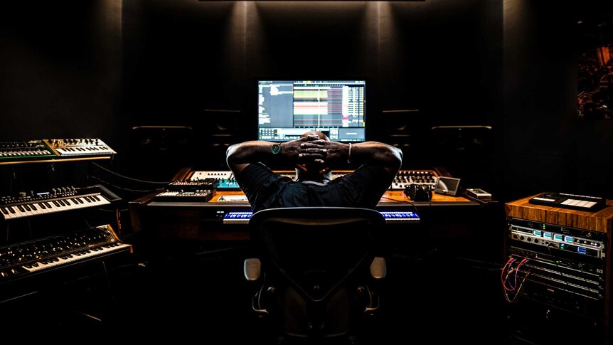 Back profile of Carl Cox at a recording studio desk, with his hands behind his head