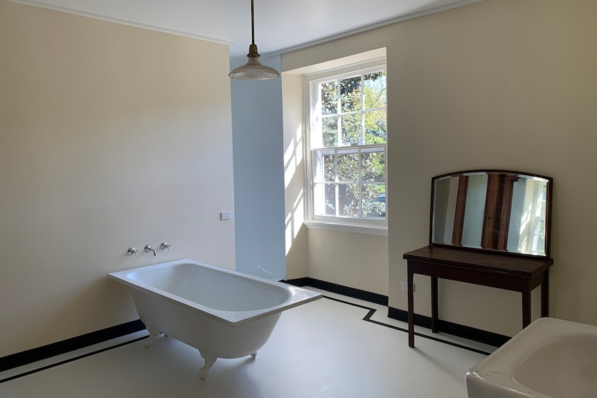 An open plan bathroom with a free standing tub against the far wall, a dressing cabinet and a sink. 