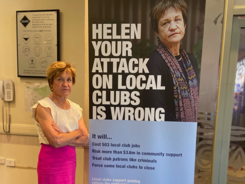 A woman with arms crossed stands next to a sign that has her photo and says 'Helen your attack on local clubs is wrong'