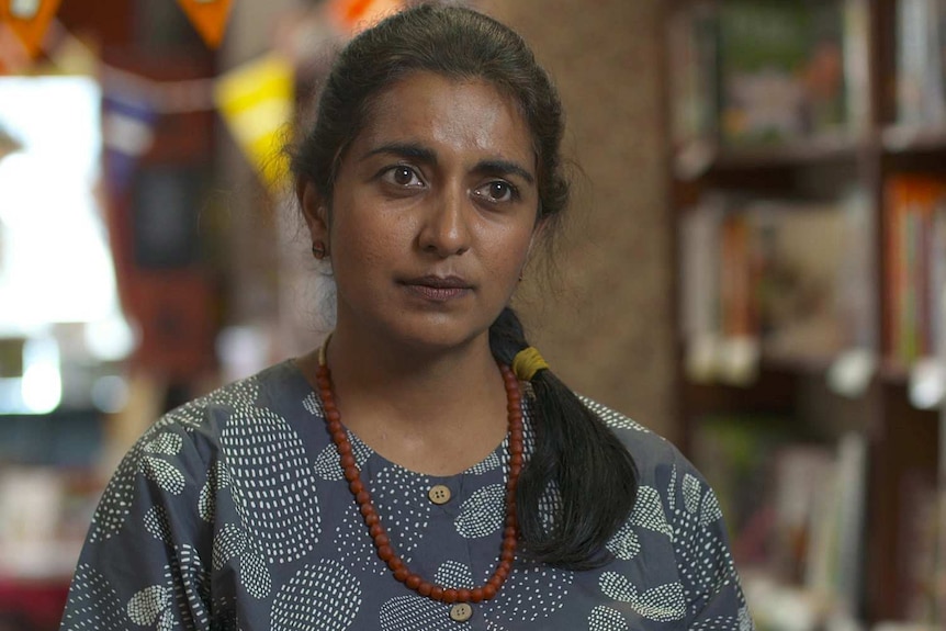 A woman wearing a blue top and brown necklace.