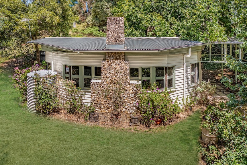 a small white weatherboard house with a stone chimney.