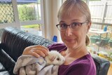 A blonde woman in her 30s wearing glasses holds a white guinea pig