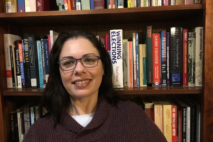 A woman in glasses in front of a bookcase of academic texts