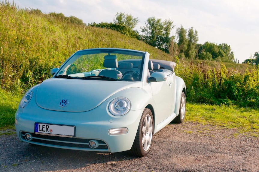 A pastel green Volkswagen New Beetle convertible is shown with its roof town parked in front of a bright green field.