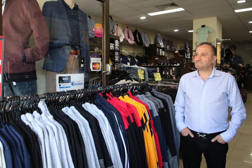 a man standing next to a rack of menswear in his store