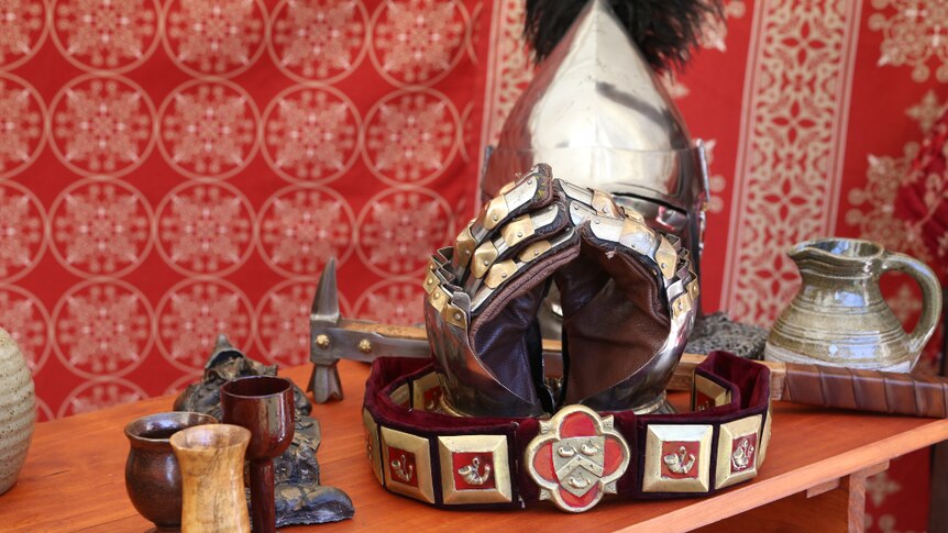 Armoured gloves, a helmet, hammer and drinking vessels are displayed in front of red cloth.