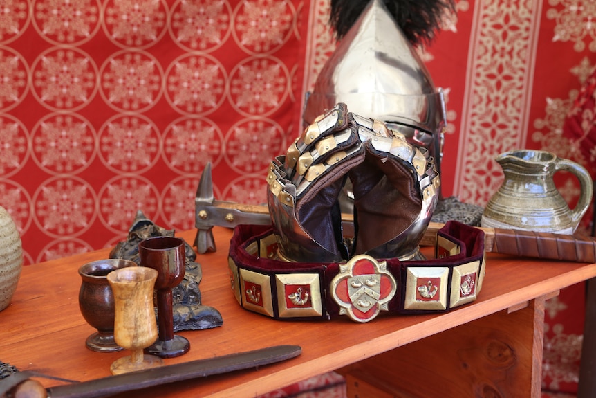 Armoured gloves, a helmet, hammer and drinking vessels are displayed in front of red cloth.