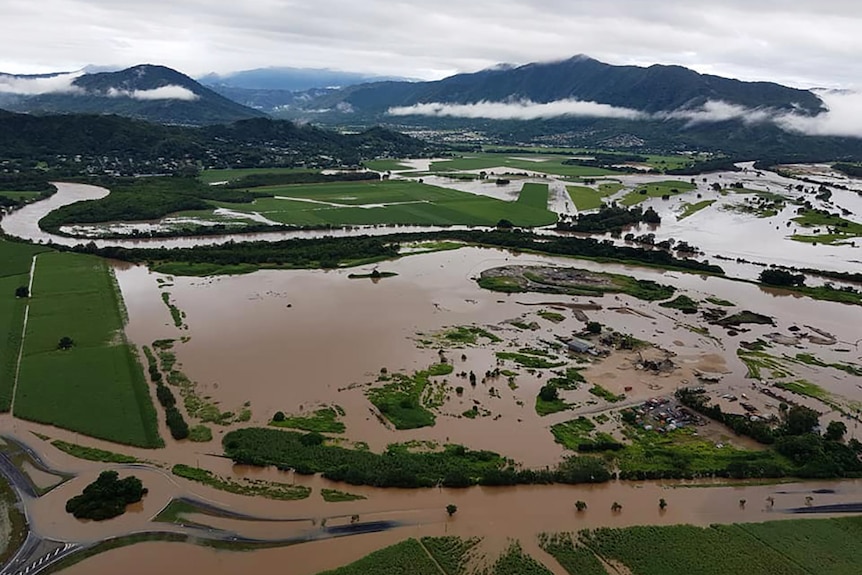 Aerial image of flooded road and farmland, mountains and clouds in the distance