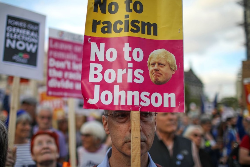 A protester holds a sign that reads "Not to racism, no to Boris Johnson".
