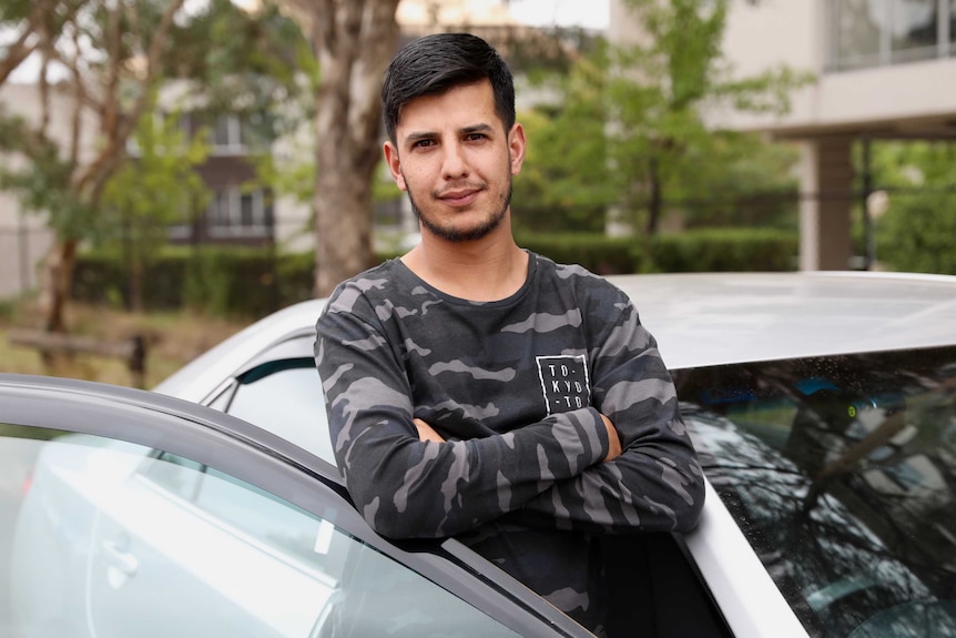 A man stands inside the open door of his car with his arms crossed.