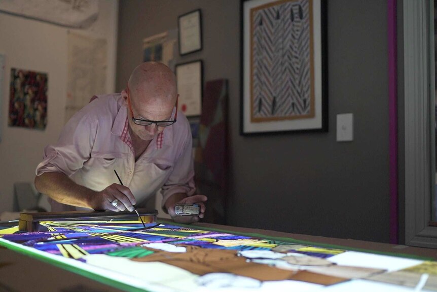 A man uses a brush to paint onto a stained glass window panel