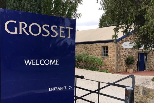A blue sign with Grosset, welcome, entrance in front of a gate and an old brick building, greenery in front and side, blue door.