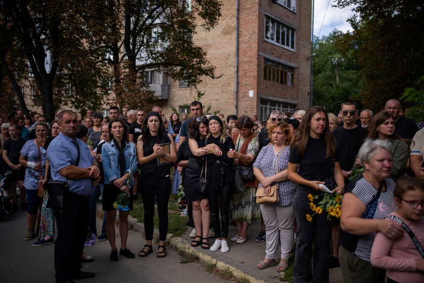 a crowd of mourners await the arrival of a coffin with Anastasiia Okhrimenko being held as she cries in the crowd