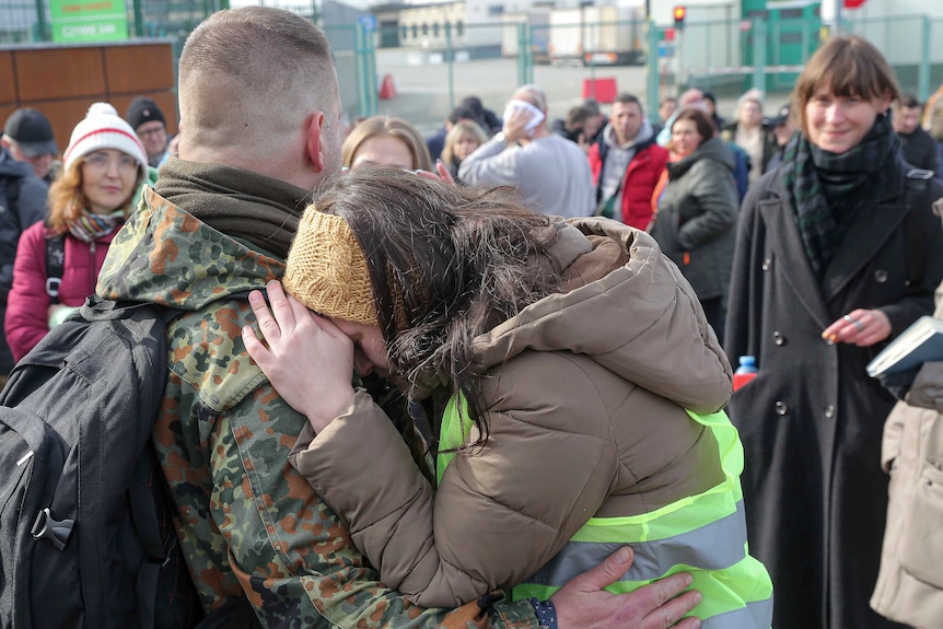 A woman hugs a man dresses in military uniform.