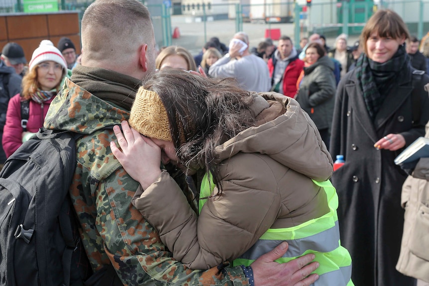 Two people hug as they stand surrounded by people.