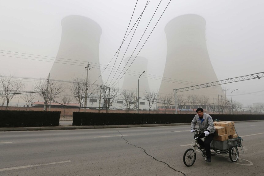 A man cycles past the water-cooling towers of a coal-fired power plant on a hazy day in Beijing.