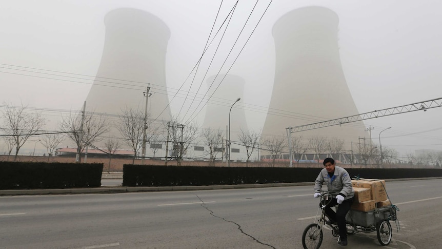 A man cycles past the water-cooling towers of a coal-fired power plant on a hazy day in Beijing.