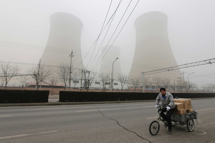 A man cycles past the water-cooling towers of a coal-fired power plant on a hazy day in Beijing.