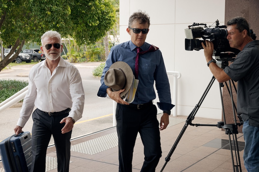 two men wearing suits and sunglasses entering court