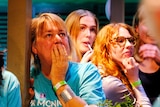 A room of women wearing teal shirts in support of Monique Ryan watch election results unfold