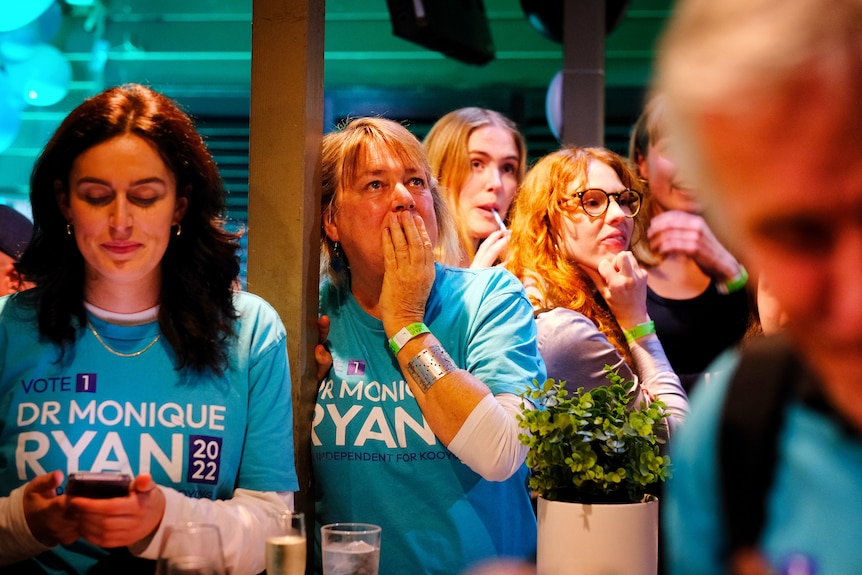 A room of women wearing teal shirts in support of Monique Ryan watch election results unfold
