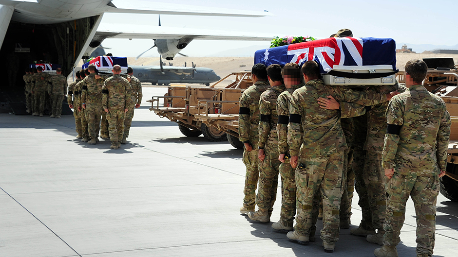 Three caskets are carried by three groups of soldiers into the back of an aircraft, on a runway at a military base