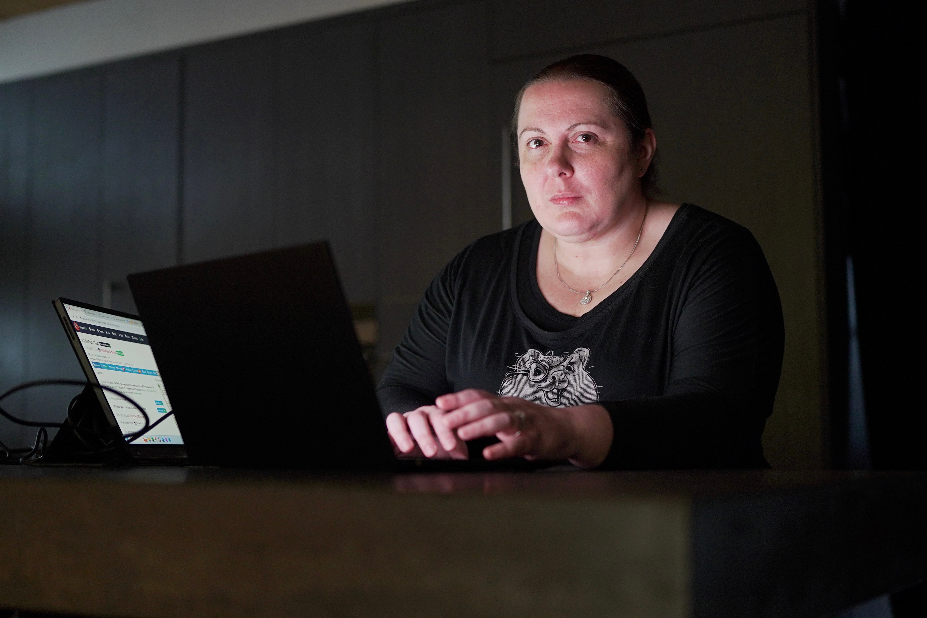 女人坐在黑暗的房间里，面前放着一台笔记本电脑。