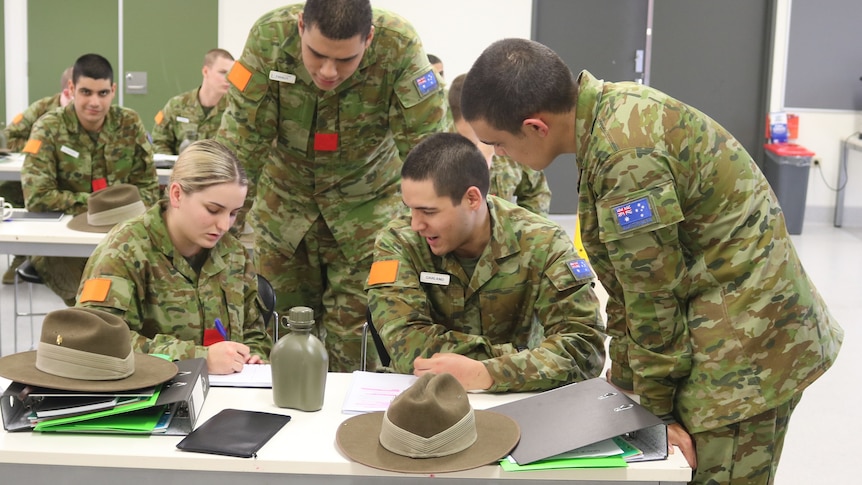 A group of people in army uniform at a desk in a classroom