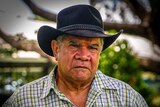 Mick Dodson stands in a park, wearing a black hat.