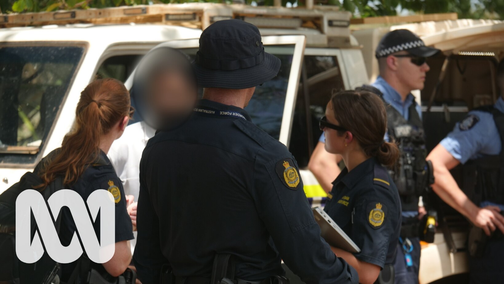 A man with a digitally blurred face talk to three people wearing Australian Border Force uniforms.