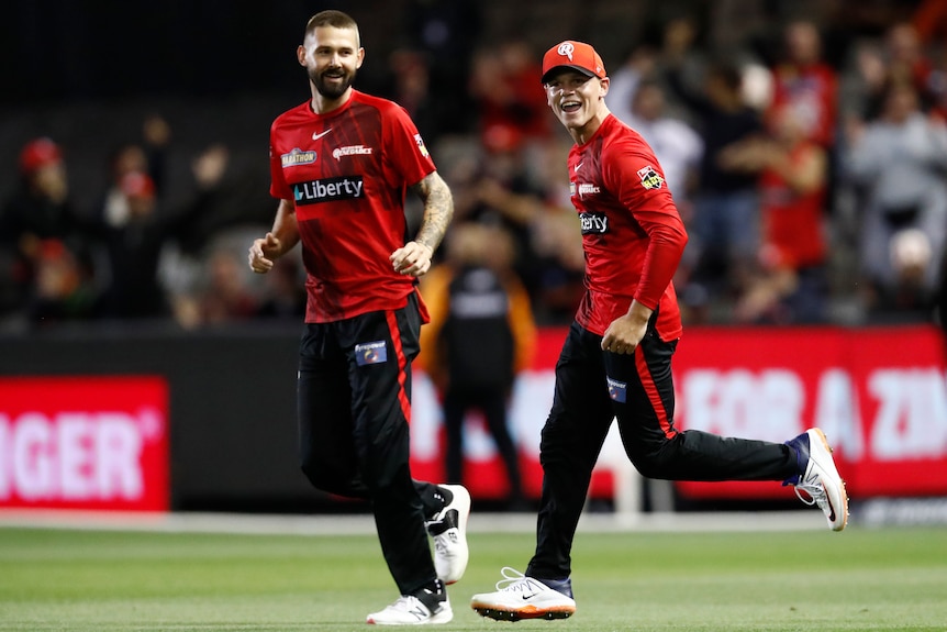 A Big Bash League cricketer jogs back from the boundary with a teammate, with a beaming smile after taking a great catch.