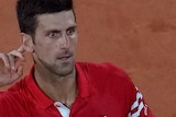 Novak Djokovic holds his hand to his ear