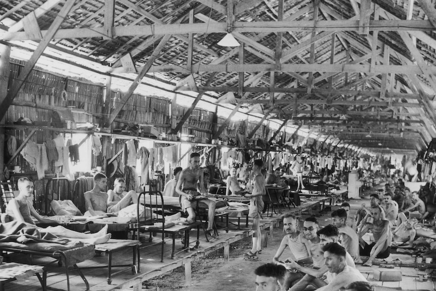 Emaciated men sit under shelter in a house