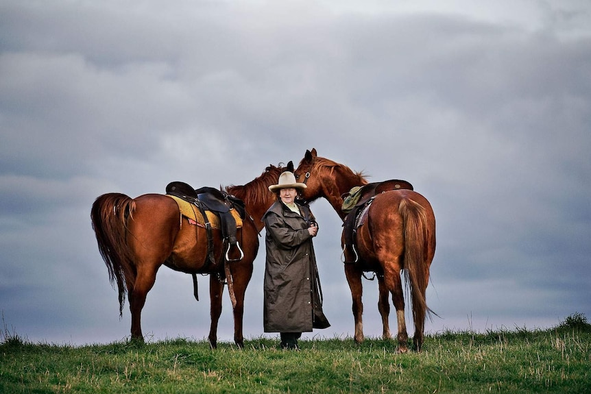 woman holding two horses on the trail