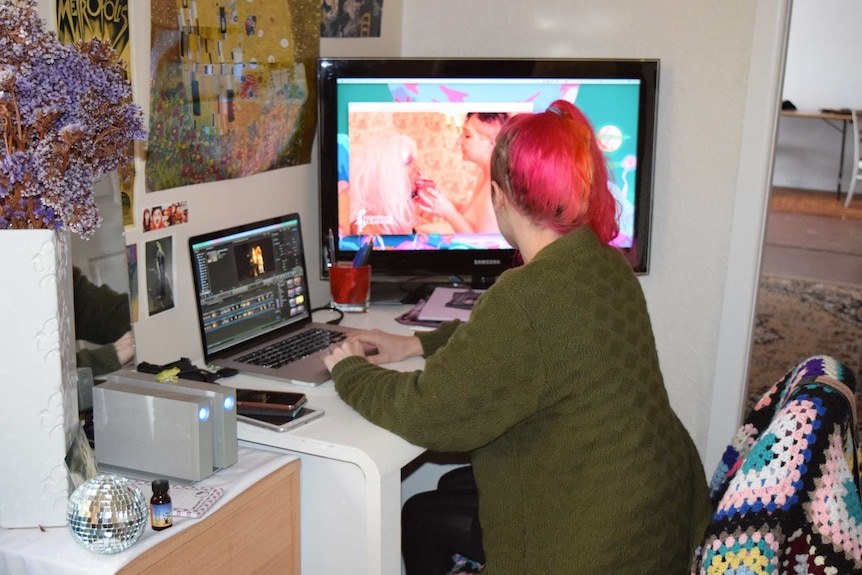 A woman sitting at a computer screen editing feminist porn.