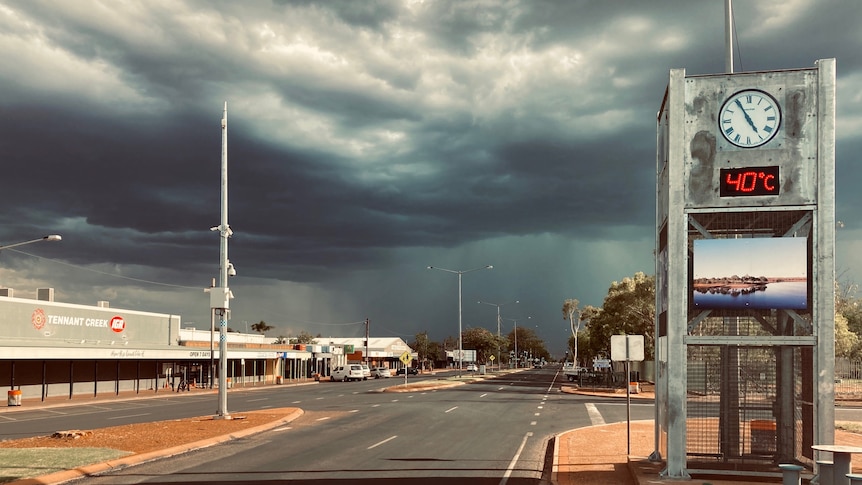 Dark rain clouds over the empty main street a clock by the side of the road says the temperature is 40 degrees celsius.