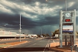 Dark rain clouds over the empty main street a clock by the side of the road says the temperature is 40 degrees celsius.