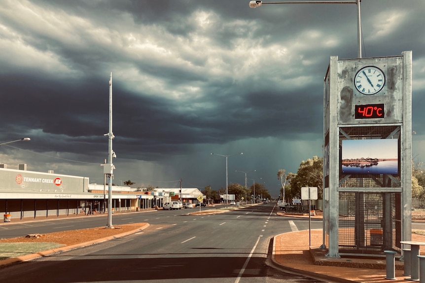 Dark rain clouds over the empty main street a clock by the side of the road says the temperature is 40 degrees celsius.