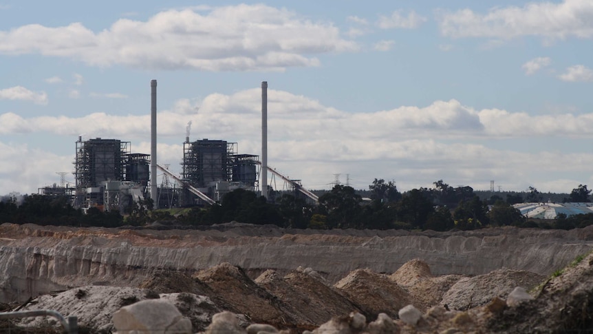 Piles of earth in an open cut coal mine with a power station in the background