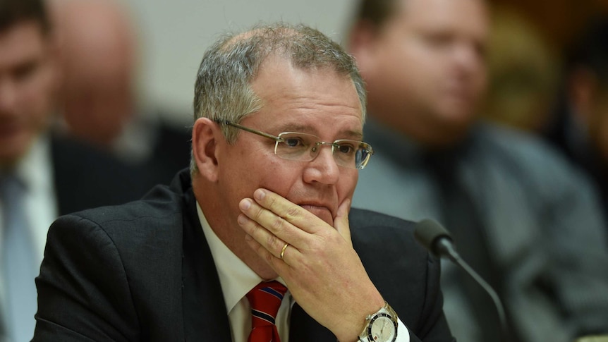 Scott Morrison rests his hand on his chin, while sitting in a Human Rights Commission hearing.