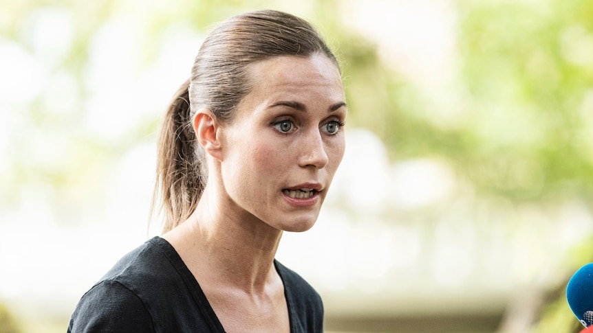 A young woman with brown hair speaks into microphones at an outdoor press conference.