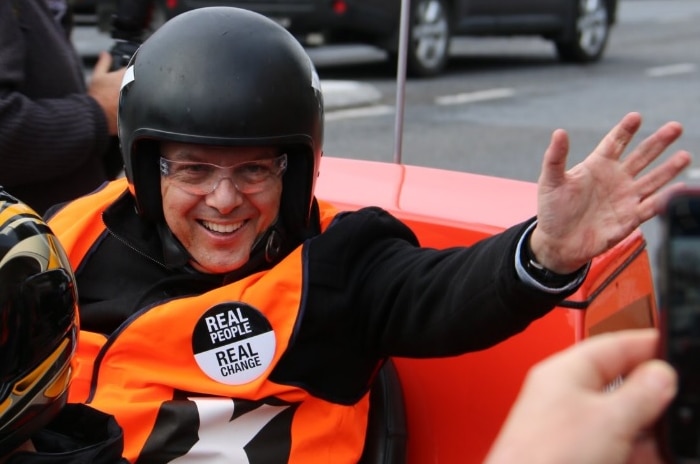 Nick Xenophon waves as he turns up on a motorbike to vote